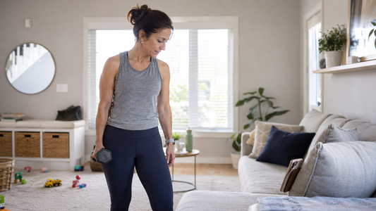 A woman in her 40s preparing to start a strength training workout in her living room at home.